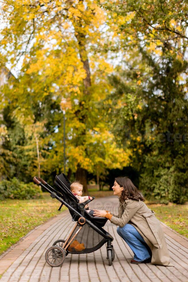 Young woman with cute baby girl in baby stroller at the autumn park photo