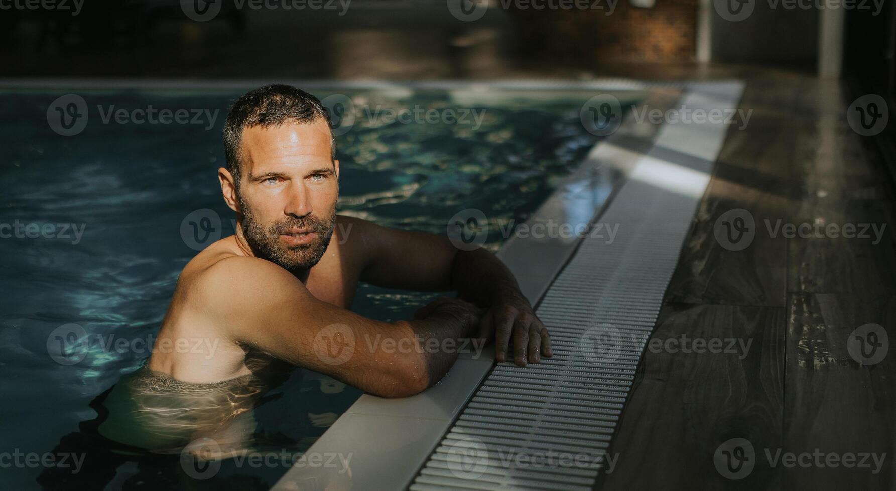 Handsome young man relaxing on the edge of indoor swimming pool photo