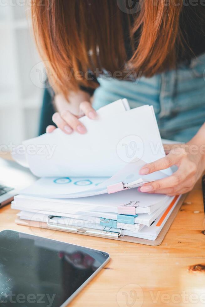 Businesswoman working in Stacks of paper files for searching and checking unfinished document achieves on folders papers at busy work desk office. photo