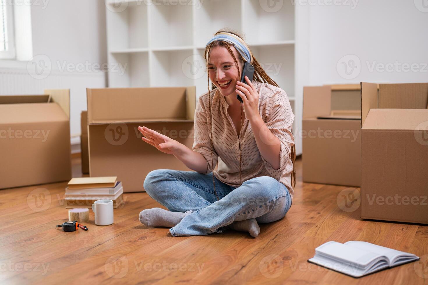 Modern ginger woman with braids talking on the phone while moving into her new apartment. photo