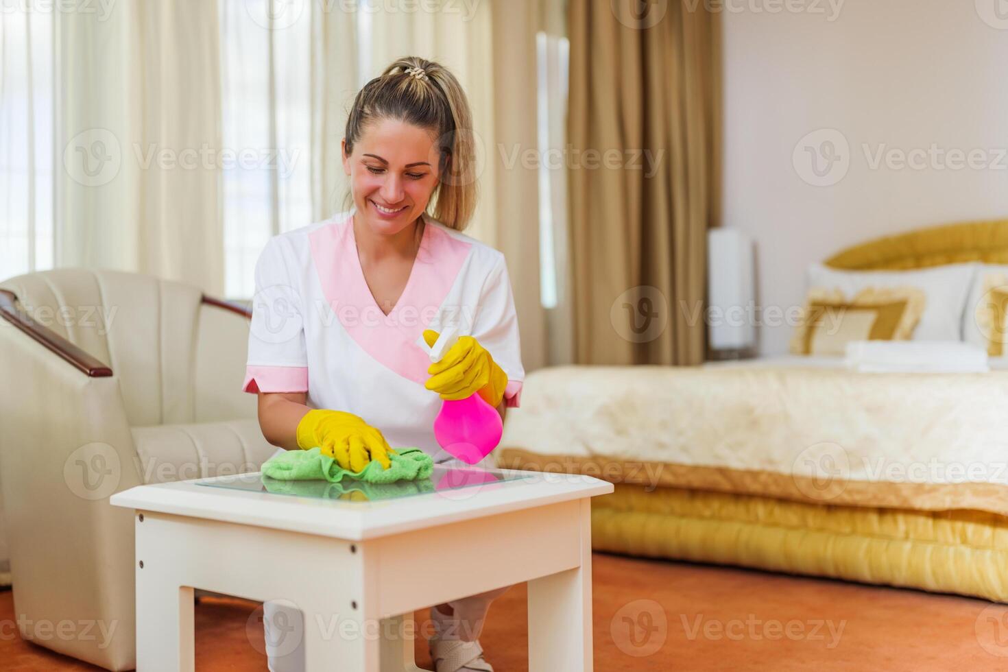 Image of beautiful hotel maid cleaning table in a room. photo