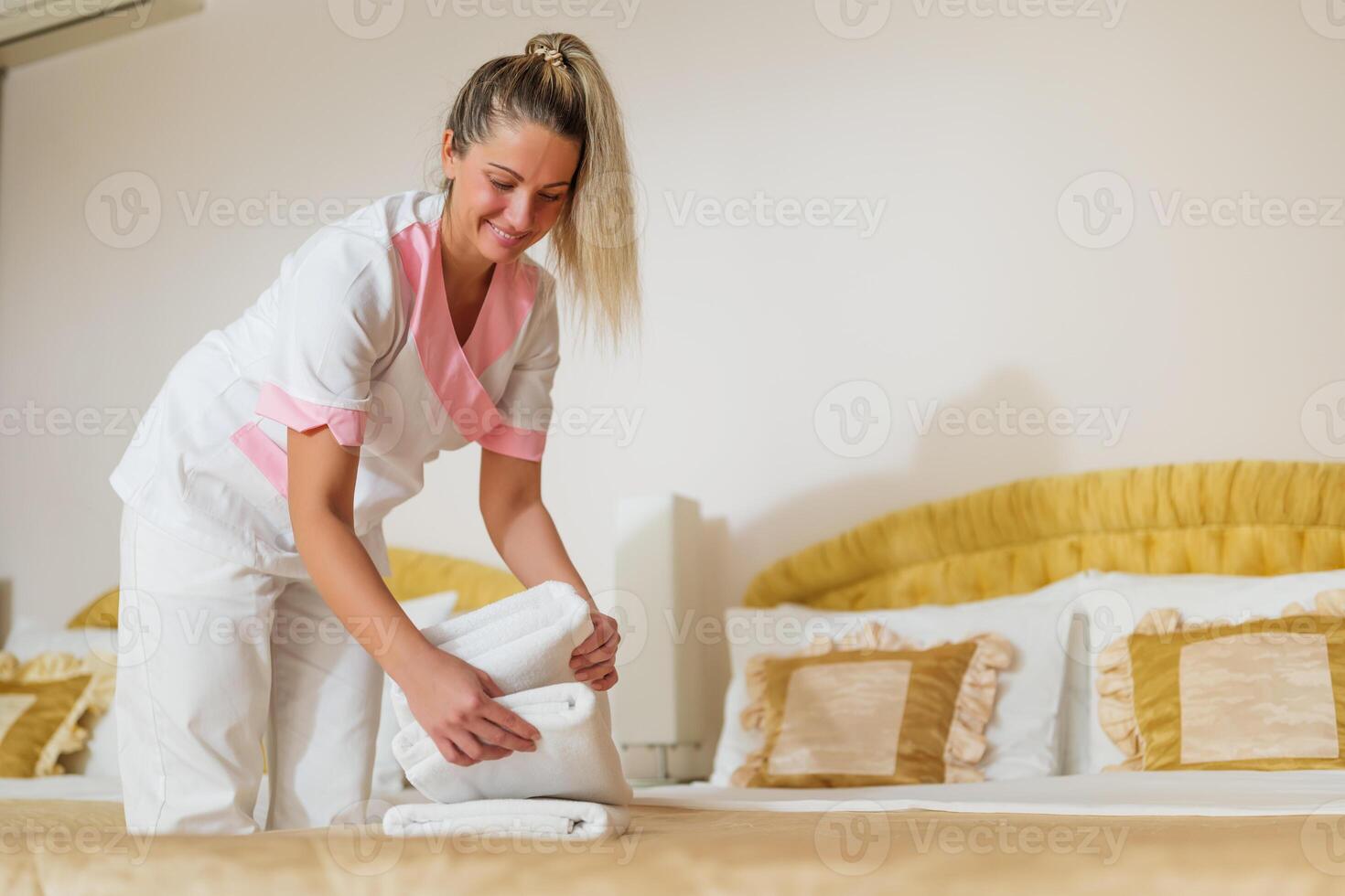 Beautiful hotel maid putting fresh and clean towels on bed in room. photo