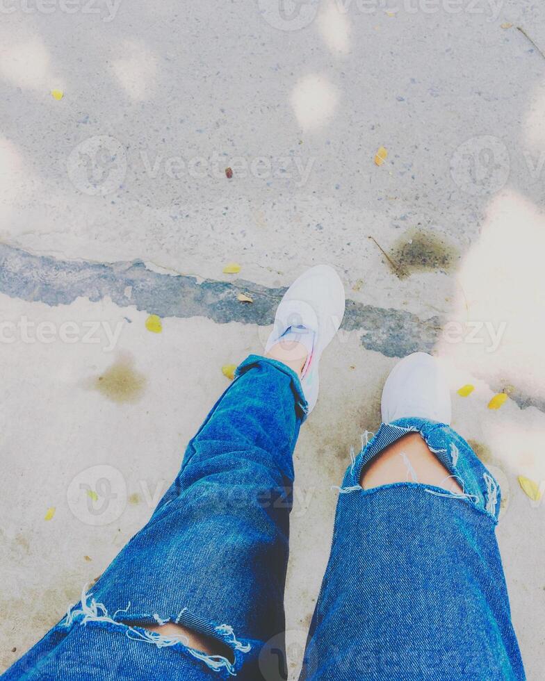 Woman's legs with blue fashion jeans and white sneakers on street photo