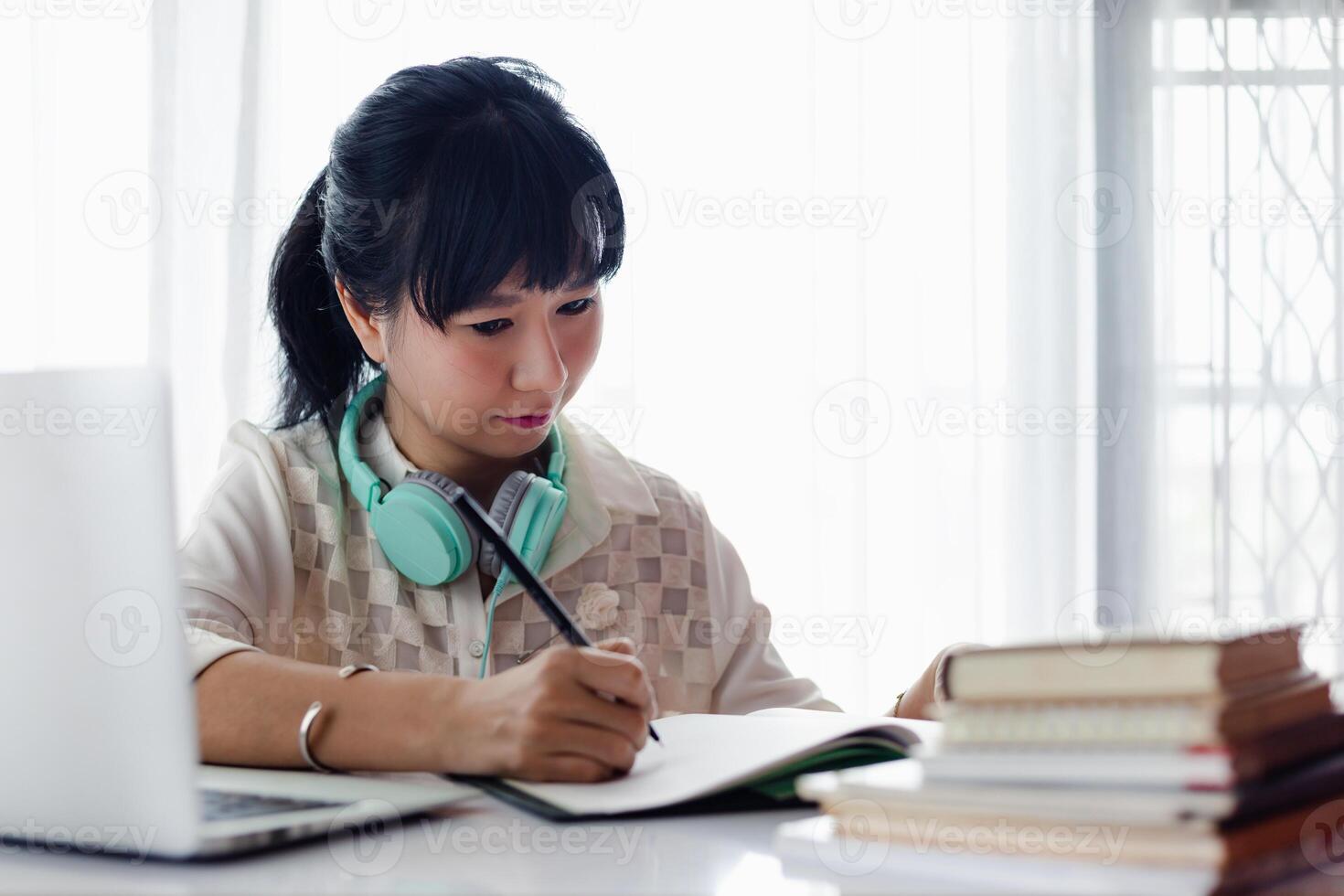 Asian woman writing on the paper, using laptop and working at home photo