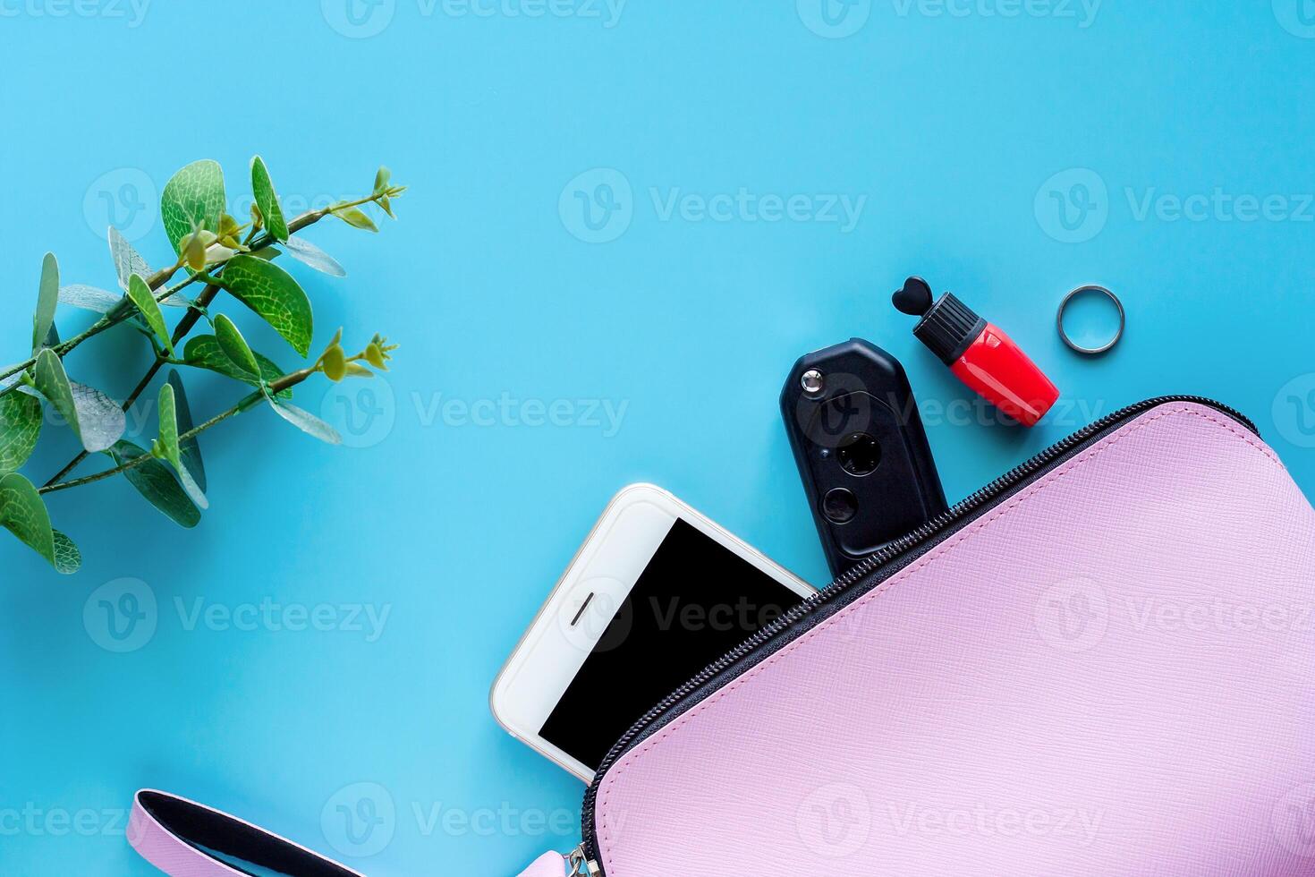 Top view of pink lady bag with smartphone, car key, red lipstick, ring and decorated flower on blue background photo