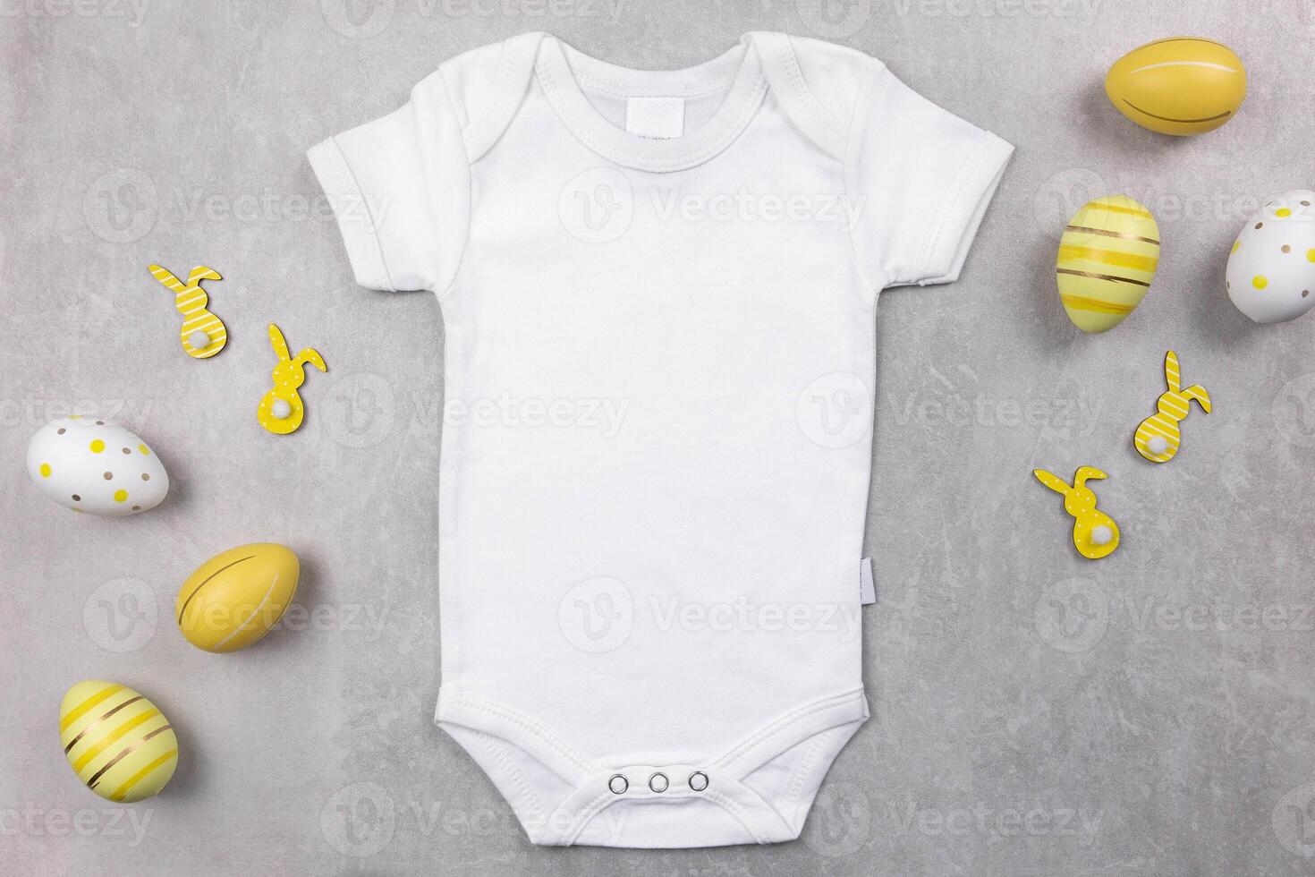 White baby girl or boy bodysuit mockup flat lay with easter eggs and bunnies decoration on the gray concrete background. Design onesie template, print presentation mock up. Top view. photo