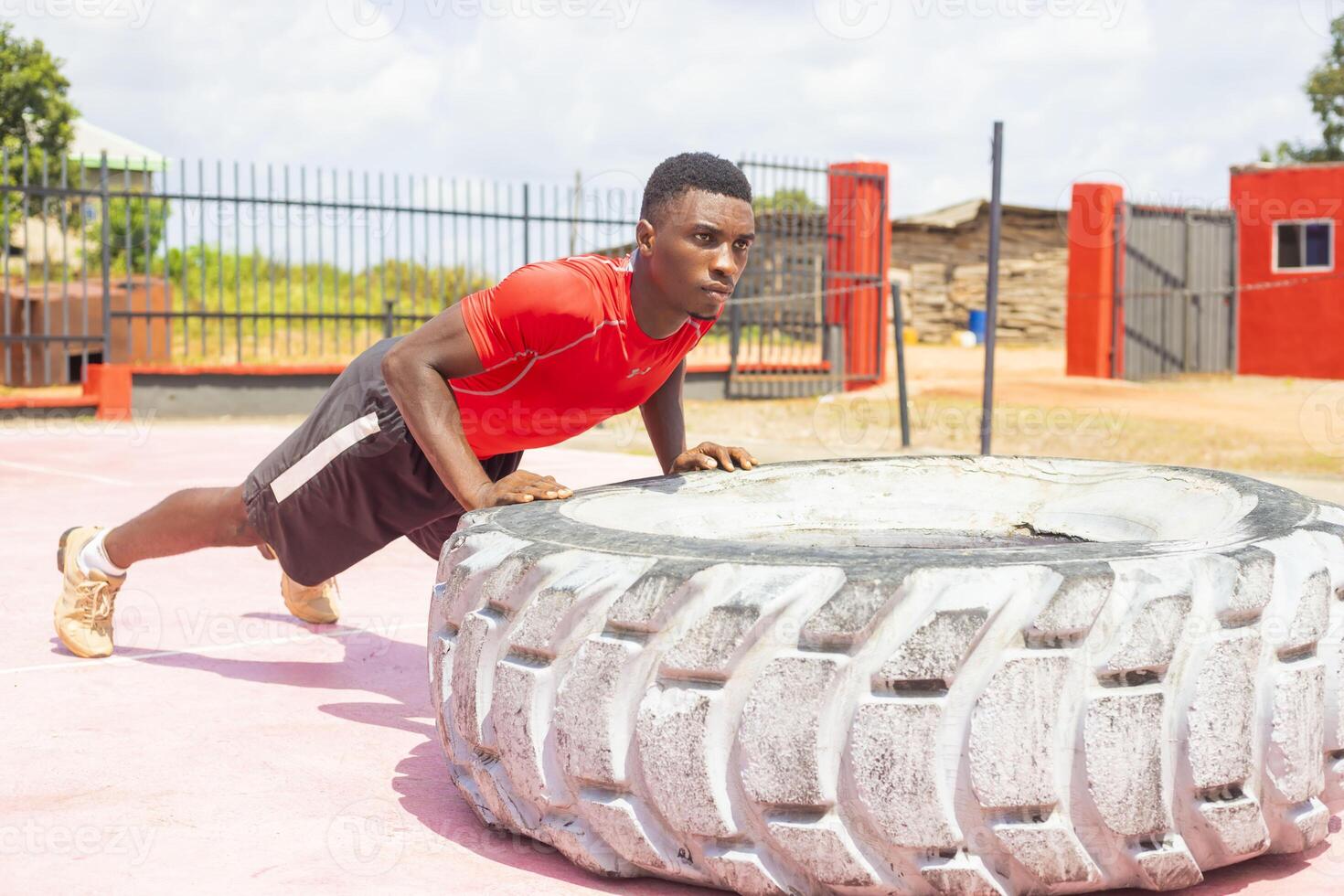 Strong sporty guy flipping workout wheel at outside gym photo