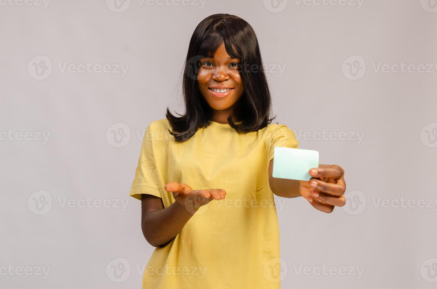 Satisfied smiling girl in stylish clothes holding bank credit card near face while standing on isolated blue background. E-banking concept photo