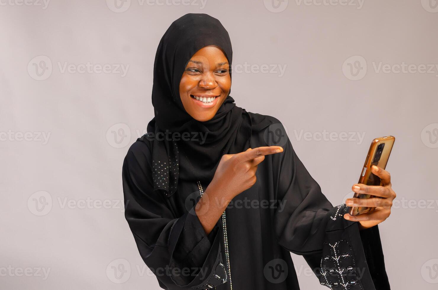 beautiful muslin lady smiling as she points to her phone. photo