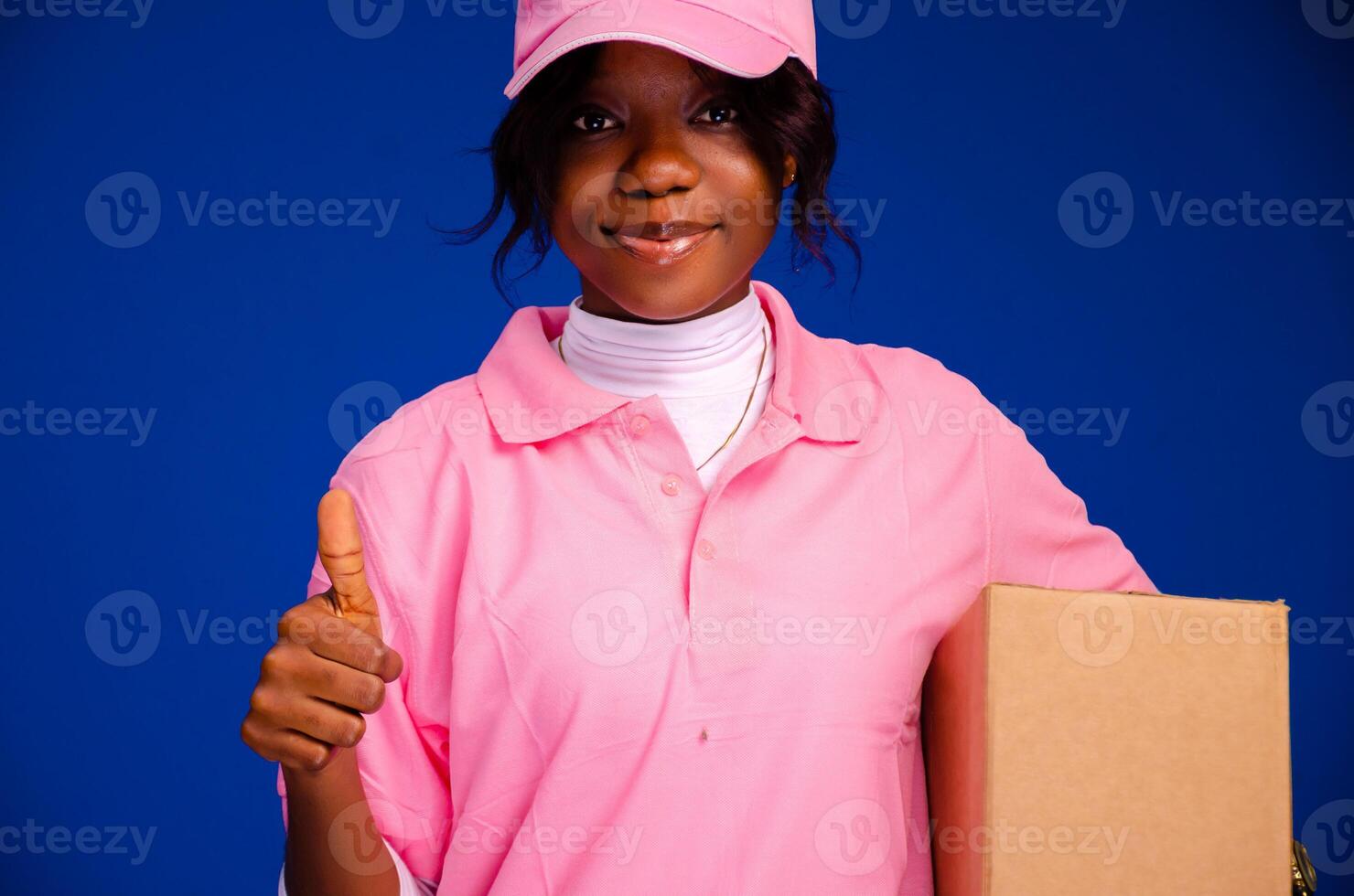 beautiful black female courier worker holding a box, does a thumbs up gesture photo