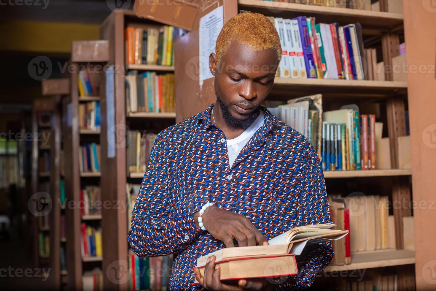 Young man reading book in library photo