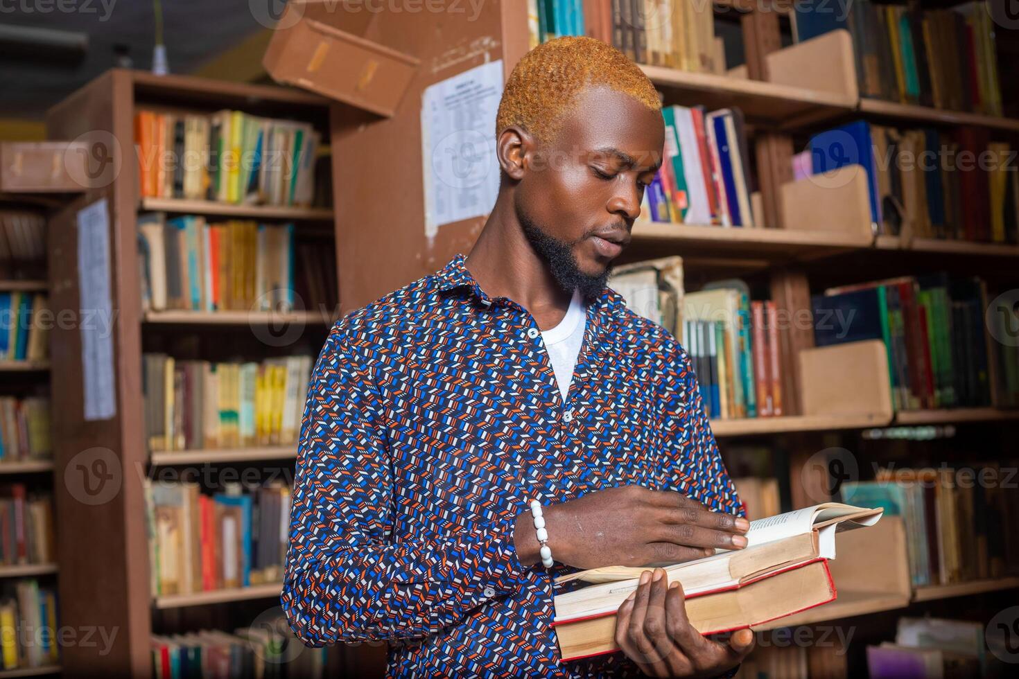 Young man reading book in library photo