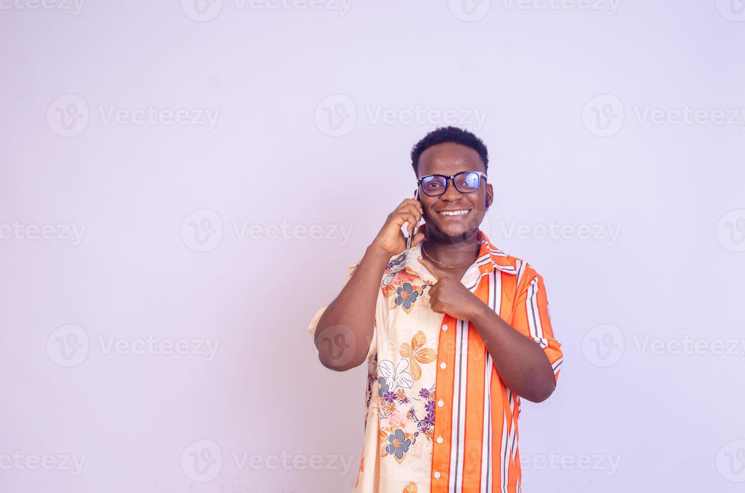 young black African boy standing on a white studio wall making calls with his mobile phone laughing out photo