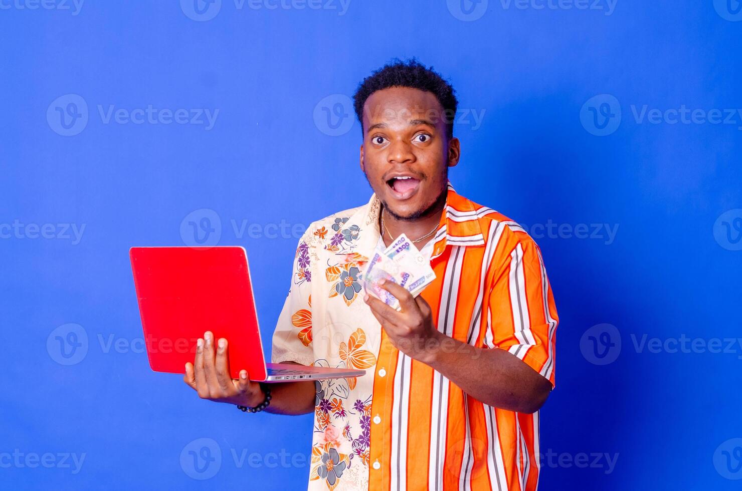 Photo of a happy young afro american handsome man posing isolated over blue wall background using laptop computer holding money.
