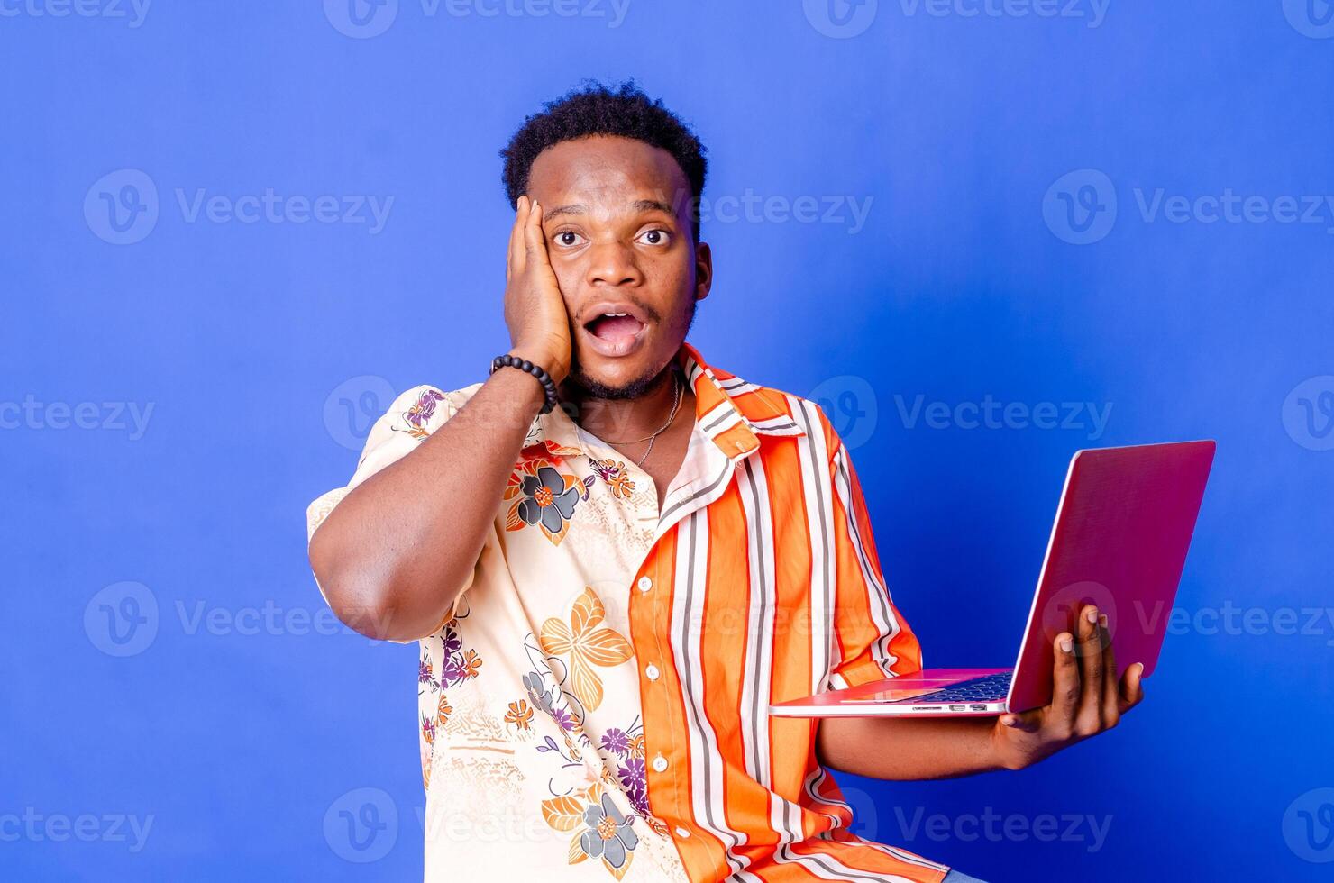 Portrait of young modern businessman standing holding laptop and looking at camera with happy smile photo
