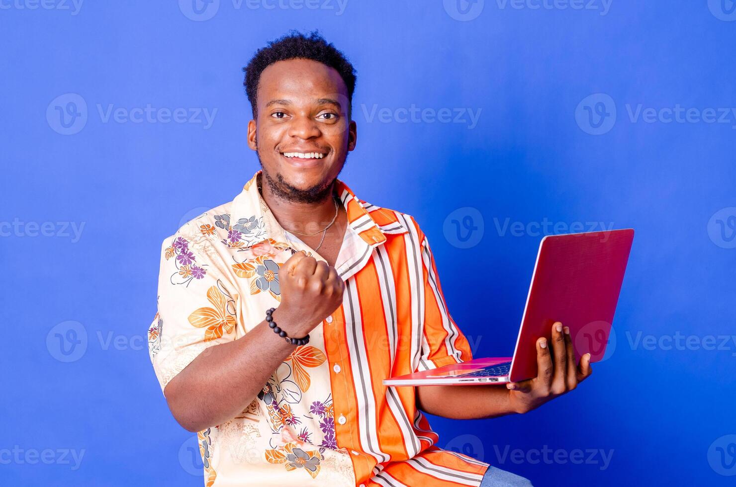 Portrait of young modern businessman standing holding laptop and looking at camera with happy smile photo