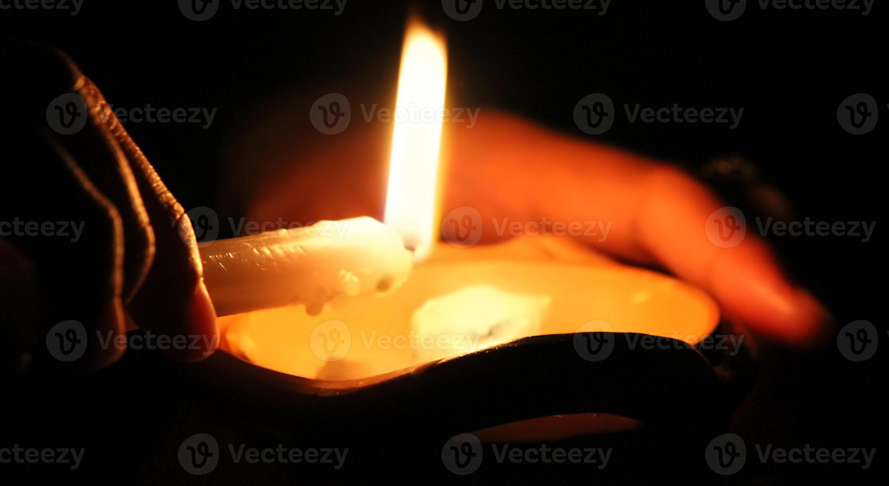 Hands holding a burning candle to drop the wax in the dark photo