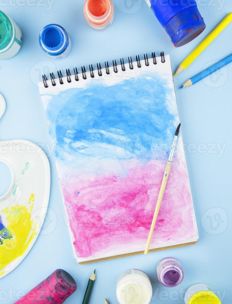 pintado cuaderno con un cepillo en un ligero azul antecedentes. artístico objetos para dibujo. plano poner. Copiar espacio. foto