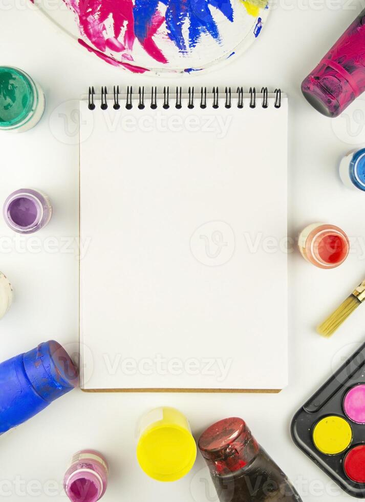 Notepad, watercolor paints and paint brushes on a white table. Flat lay. Copy space. photo