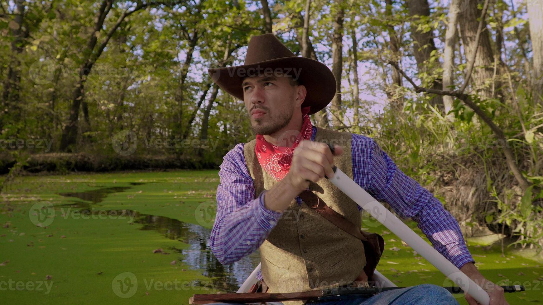 A cowboy in a red canoe floats on green river in the forest. Historical reconstruction of life in the wild west of America. photo