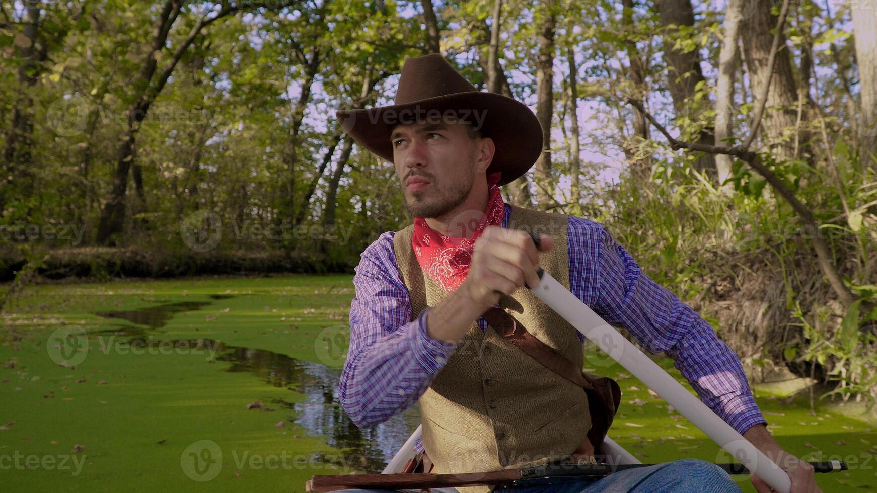 un vaquero en un rojo canoa flotadores en verde río en el bosque. histórico reconstrucción de vida en el salvaje Oeste de America. foto