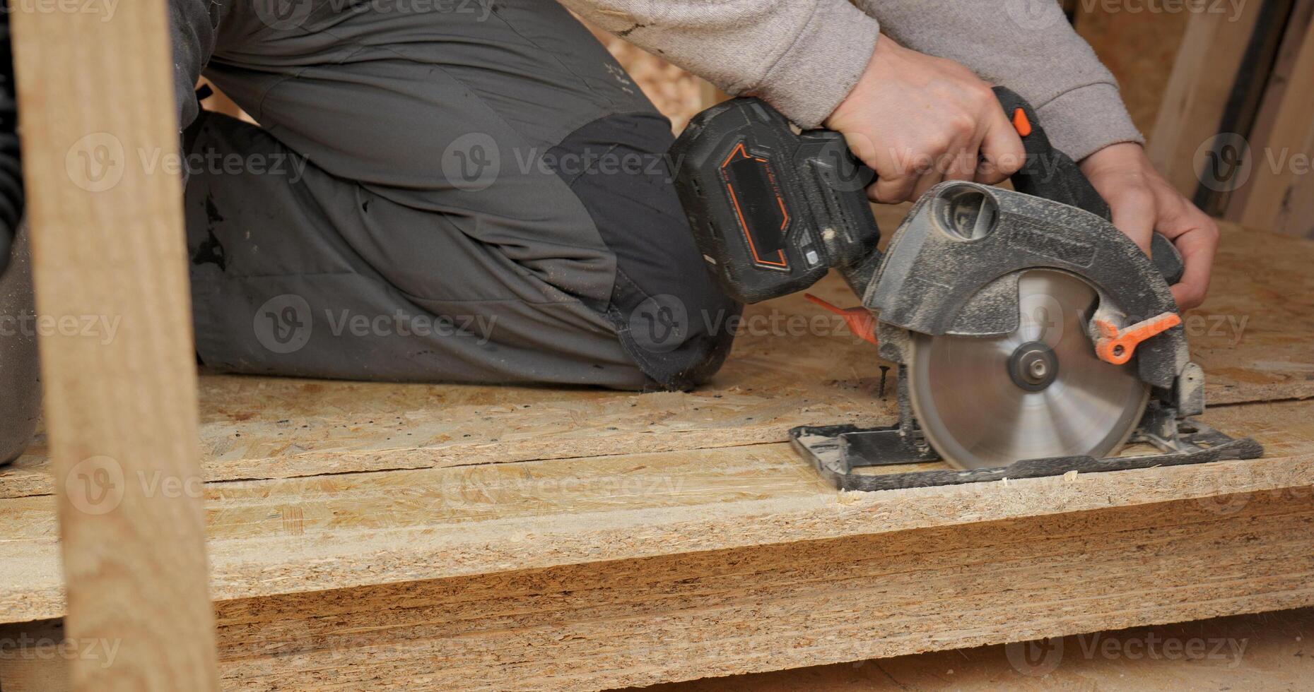 Close-up of a worker's hands using a circular saw to cut plywood. Construction of a new wooden house using frame technology. Carpentry and construction concept. photo