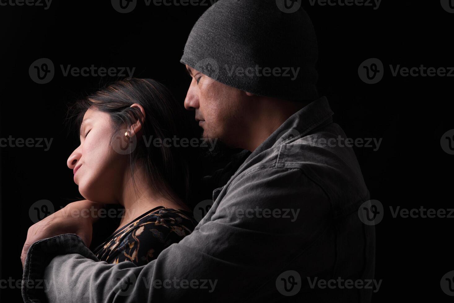 Man hugs woman from behind on a dark background and she reciprocates. photo