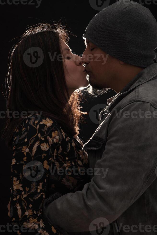 Couple kiss on a dark background with a light that borders their silhouette. photo