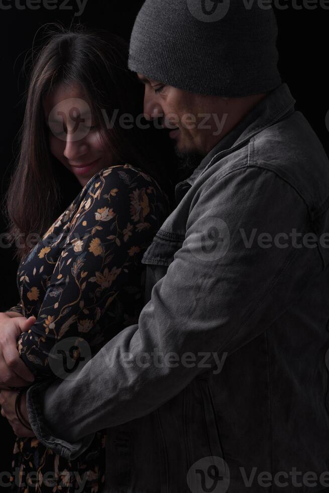 Man hugs woman from behind on a dark background and she reciprocates. photo