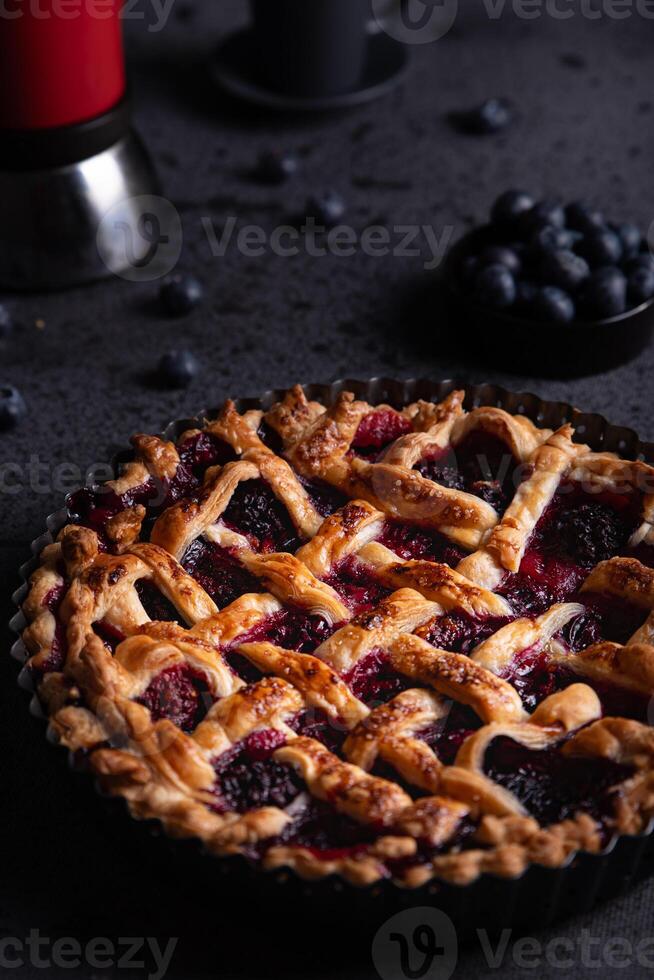 Red fruit cake, blueberries and a coffee pot placed on a dark background. photo