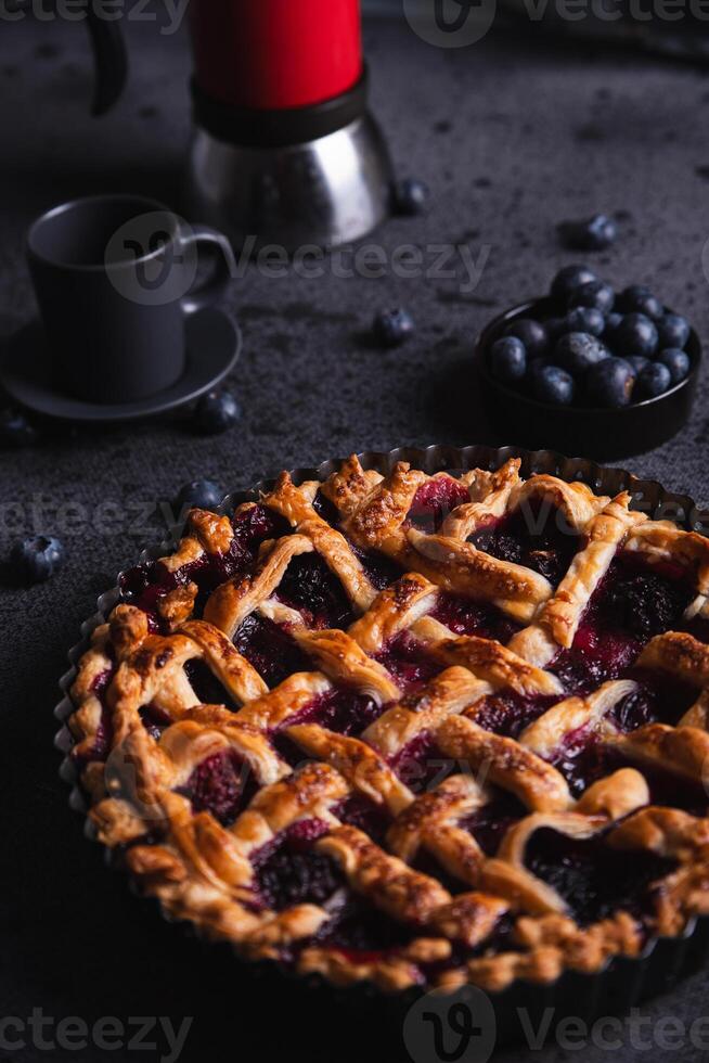 Red fruit cake, blueberries and a coffee pot placed on a dark background. photo