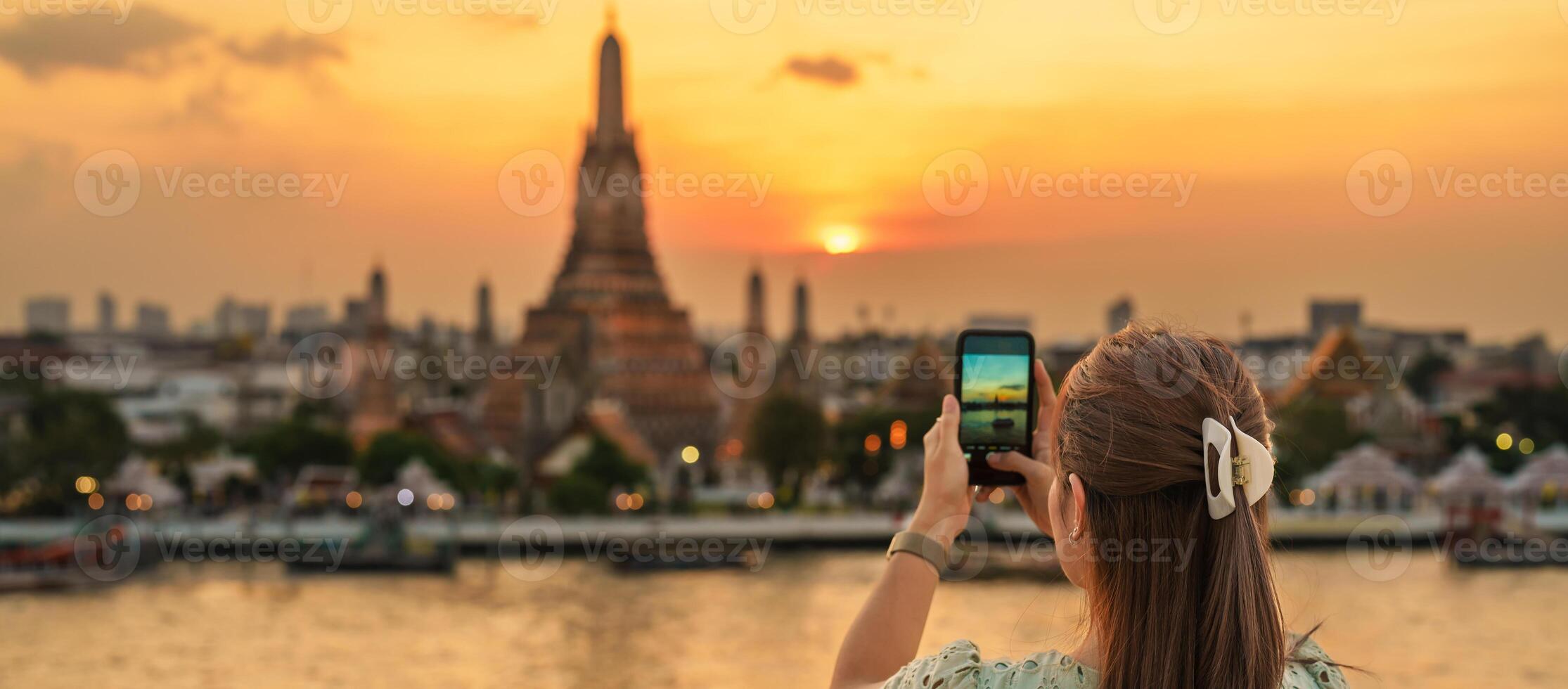 turista mujer disfruta ver a wat arun templo en atardecer, viajero tomar foto a templo de amanecer por teléfono inteligente desde techo bar. punto de referencia y viaje destino en bangkok, Tailandia y Sureste Asia