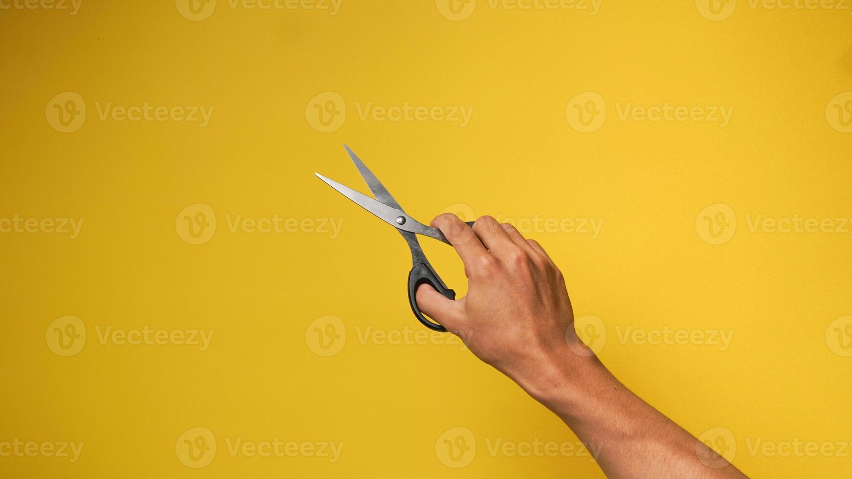 Man's hand holding black scissors on a yellow background photo