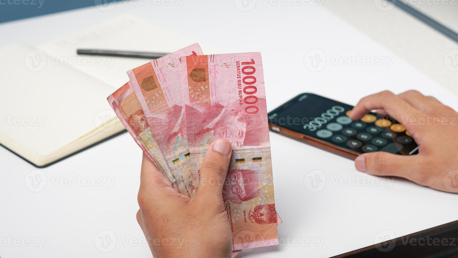 a man is counting Indonesian rupiah banknotes with a calculator. financial management concept photo