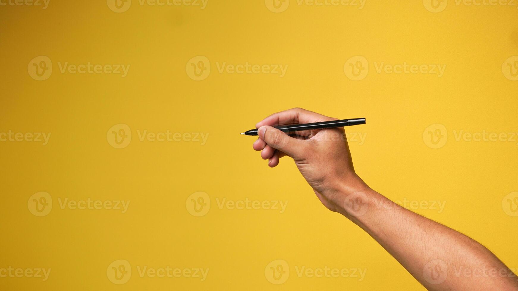 Hand of man holding pen on yellow background photo