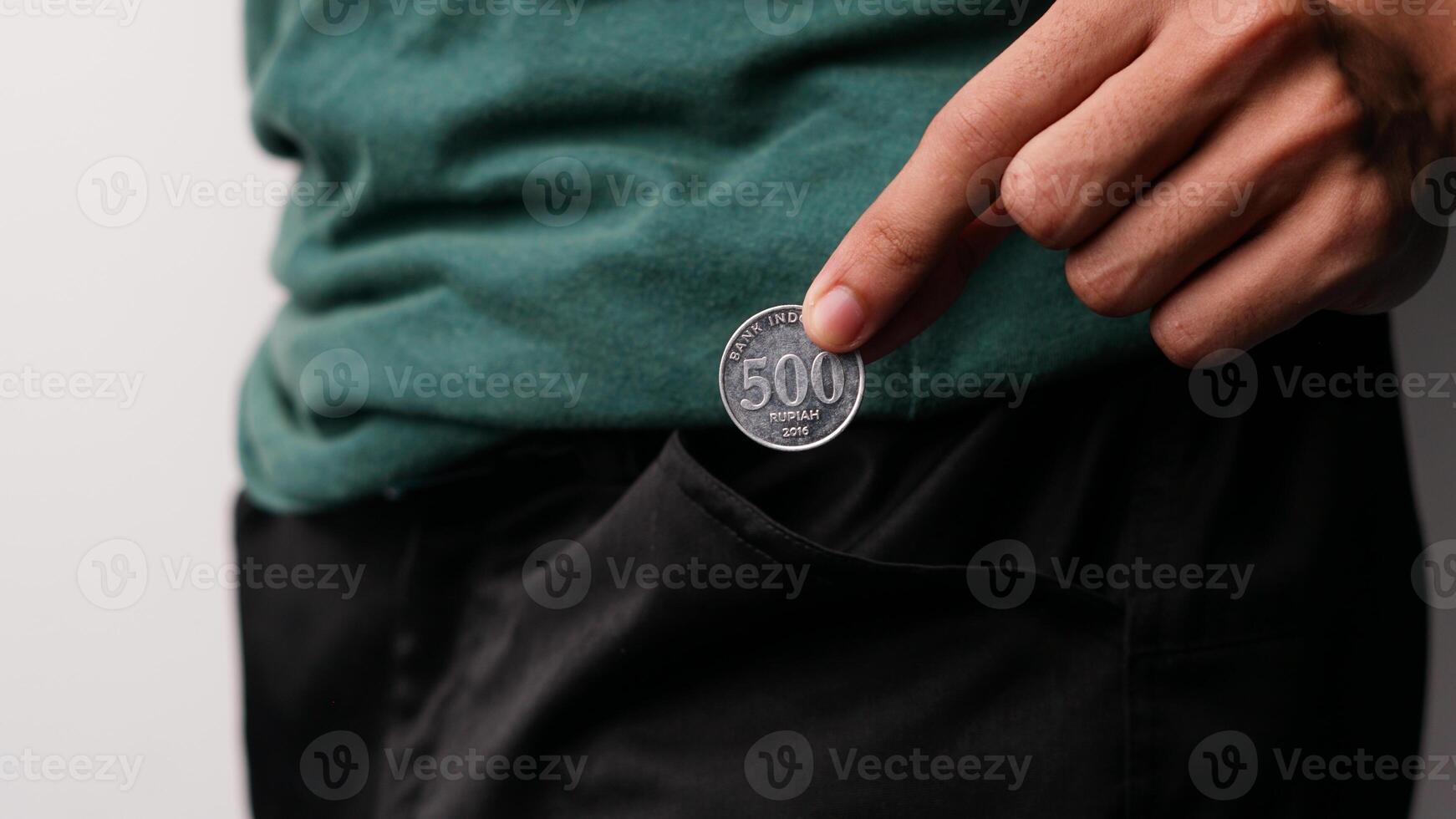 un del hombre mano es poniendo 500 rupia monedas en su pantalón bolsillo para ahorros foto