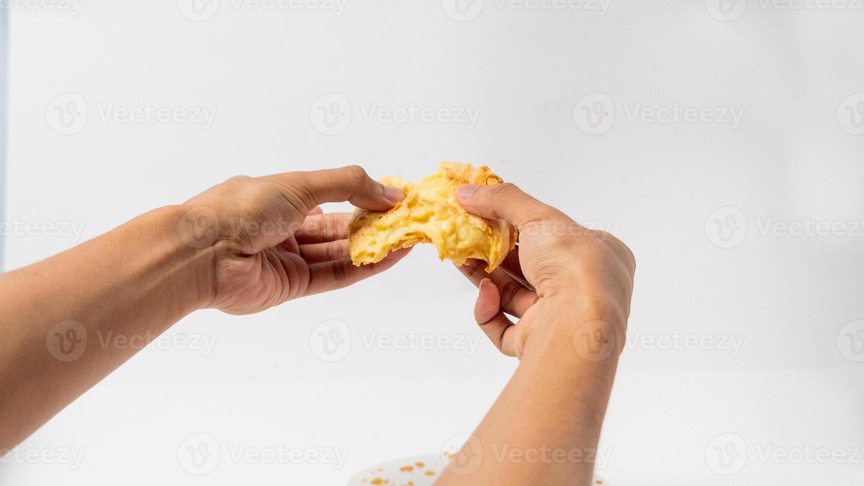 two hands are splitting a Vanilla eclair isolated on a white background photo