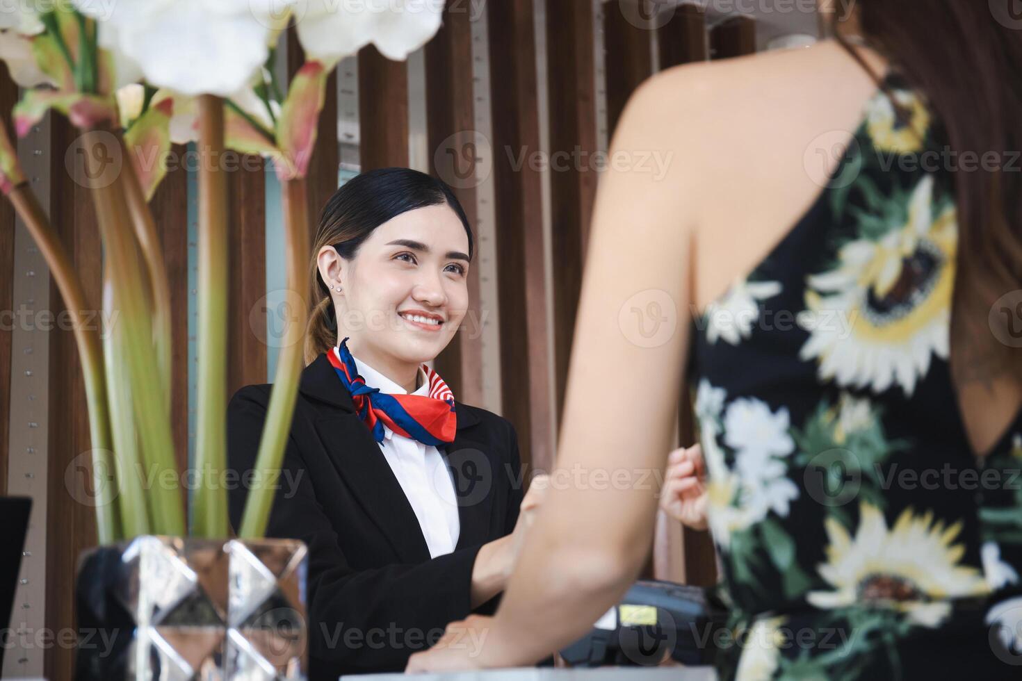 joven asiático mujer recepcionista a el hotel mostrador hablando con borroso hembra viajeros registrarse a el hotel, hembra recepcionista trabajando en el hotel foto