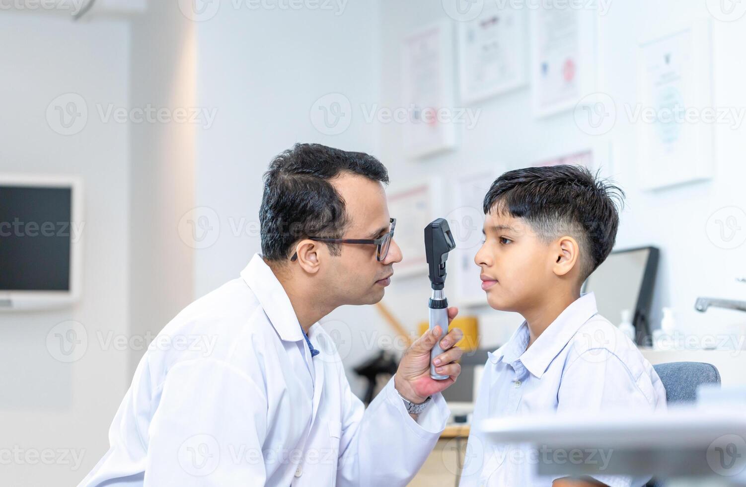 Optometrist doing sight testing for child patient in clinic, Indian child choosing eyeglasses in optics store, Boy doing eye test checking examination with optometrist in optical shop photo