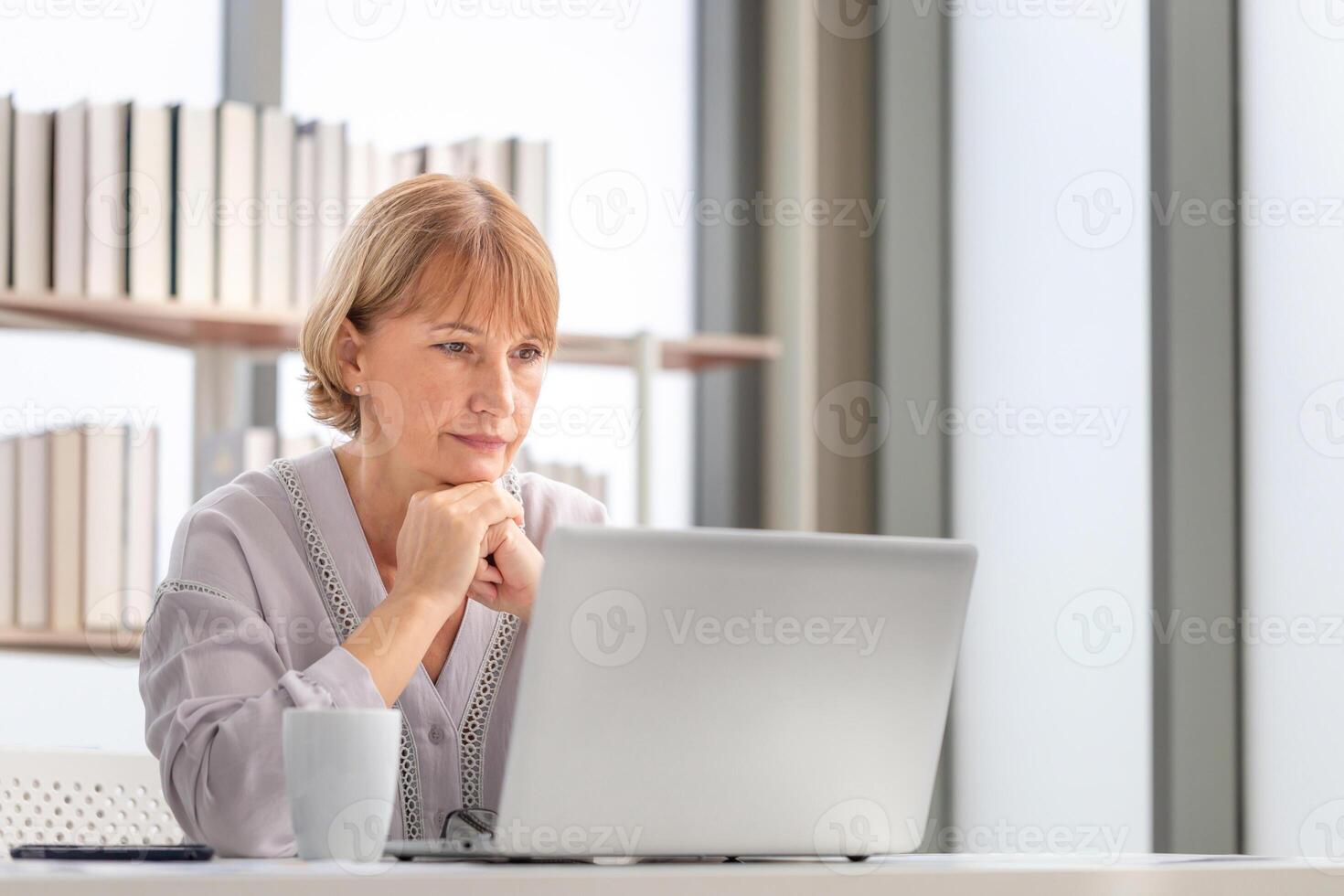 Mature women using laptop computer checking their bills, Woman reading documents, Mature woman in living room with laptop photo