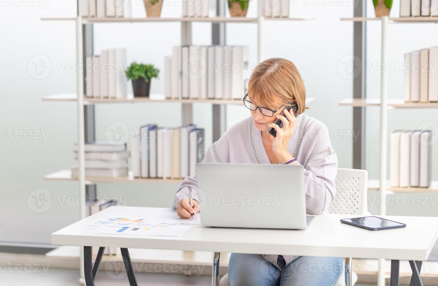 Mature women using laptop computer checking their bills, Woman reading documents, Mature woman in living room with laptop photo