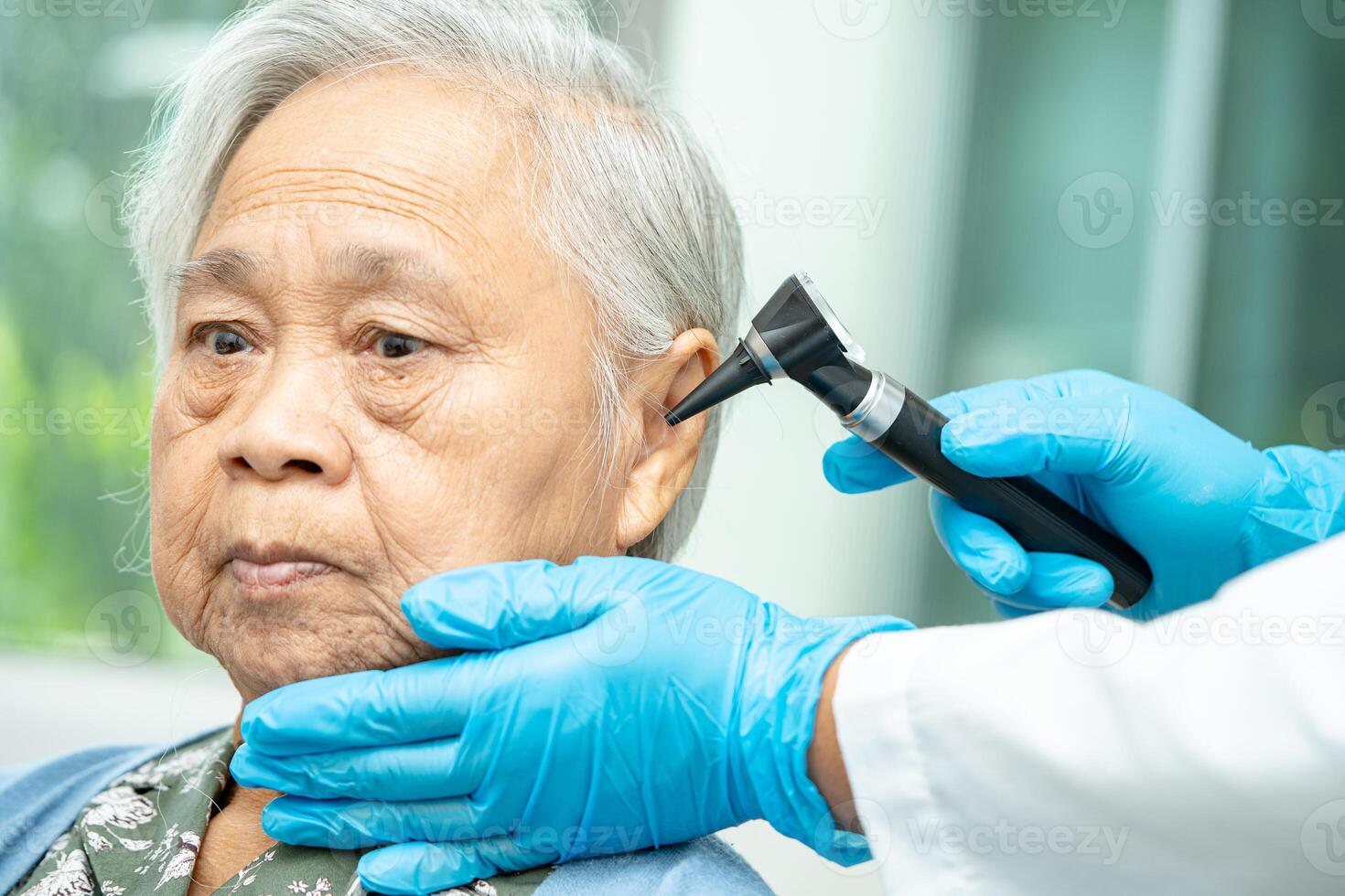 Audiologist or ENT doctor use otoscope checking ear of asian senior woman patient treating hearing loss problem. photo