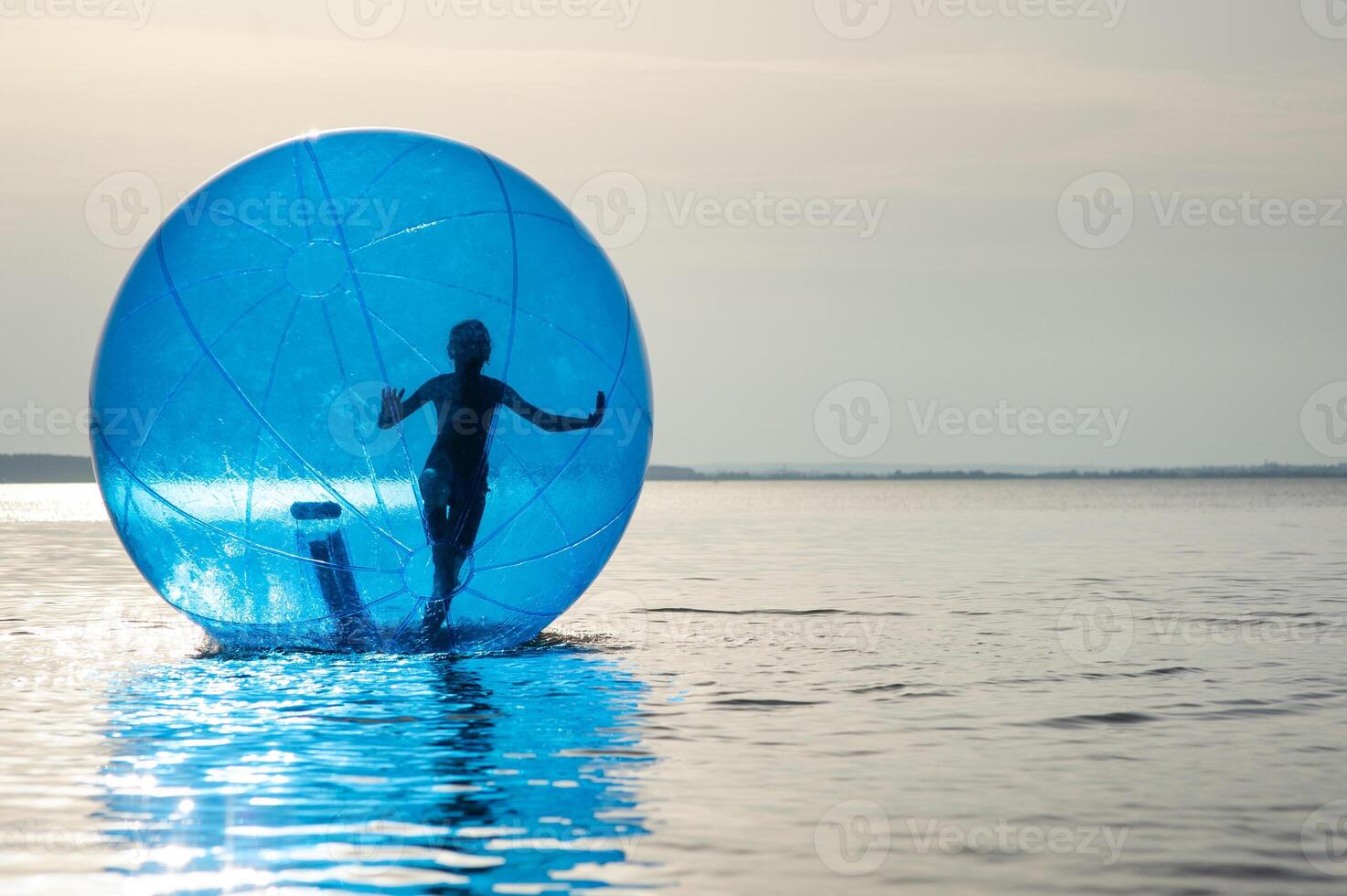 un niña en un inflable atracción en el formar de un pelota en el mar foto