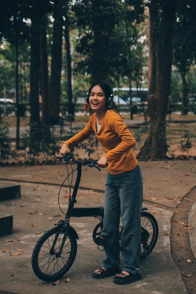 Happy young Asian woman while riding a bicycle in a city park. She smiled using the bicycle of transportation. Environmentally friendly concept. photo