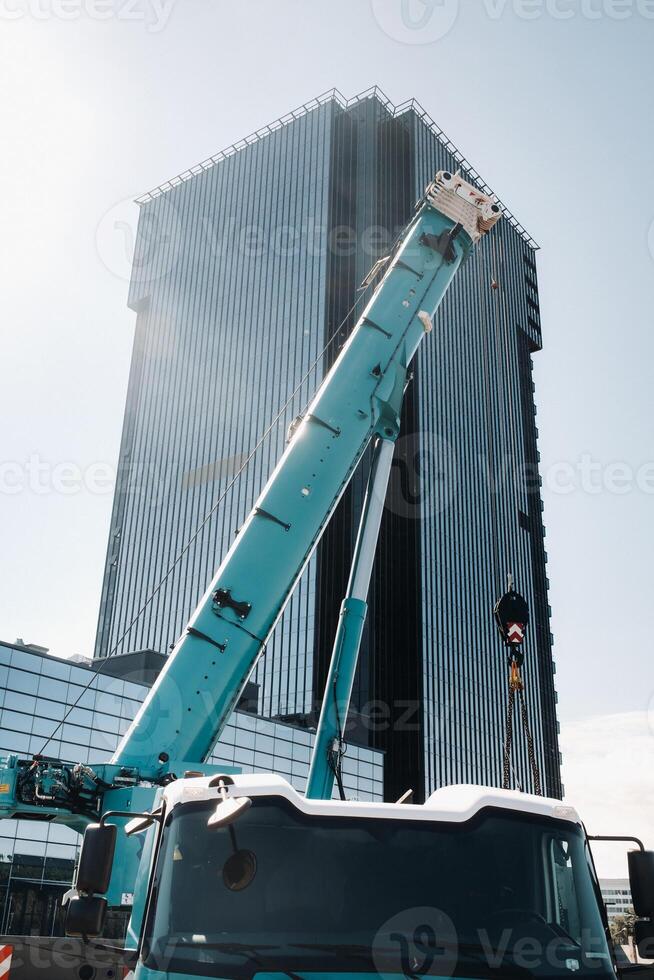 blue crane lifting mechanism with hooks near the glass modern building, crane and hydraulic high lift up to 120 meters photo