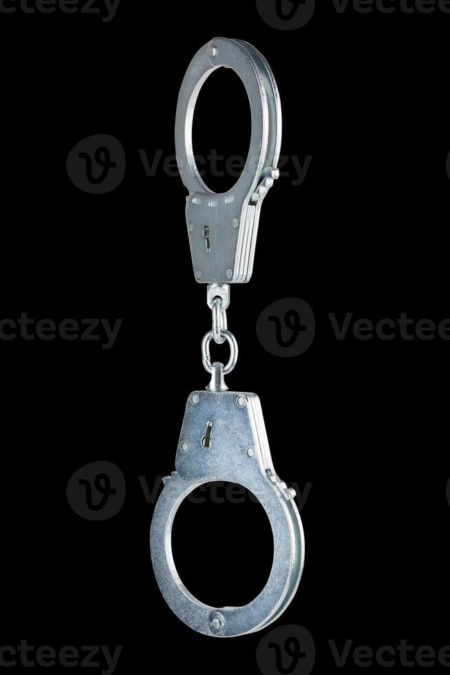 real zinc plated steel police handcuffs closed hanging vertically, isolated on black background photo