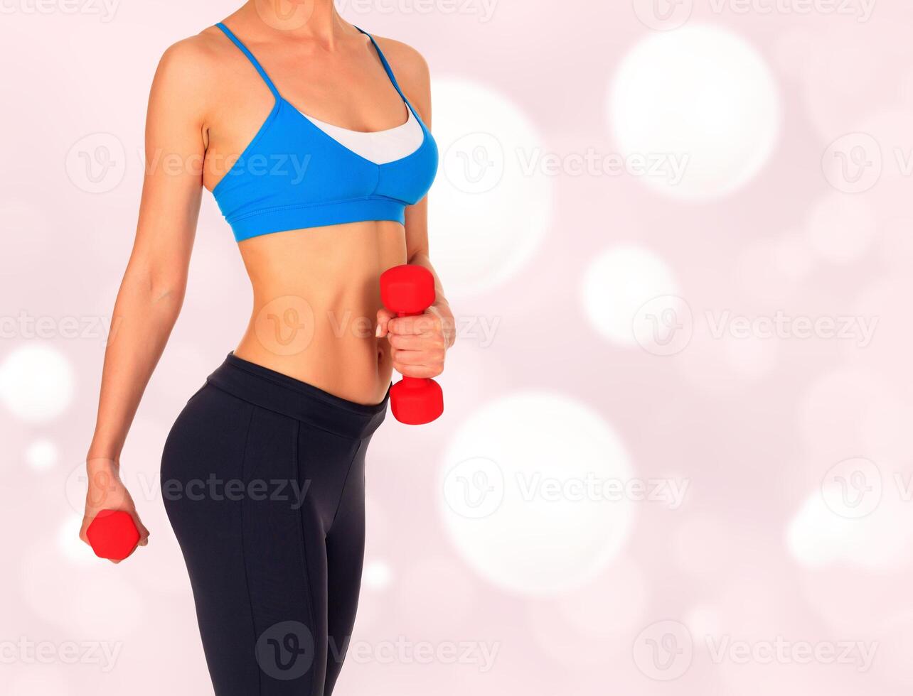 Beautiful body of a young fit slim woman lifting dumbbells against an abstract background photo