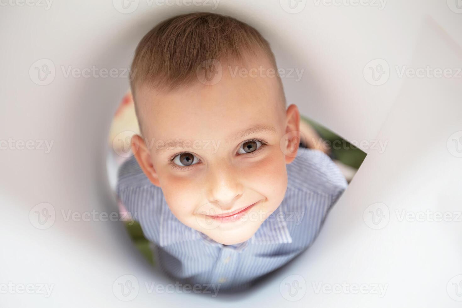 The face of a funny little boy looking into a paper hole. photo