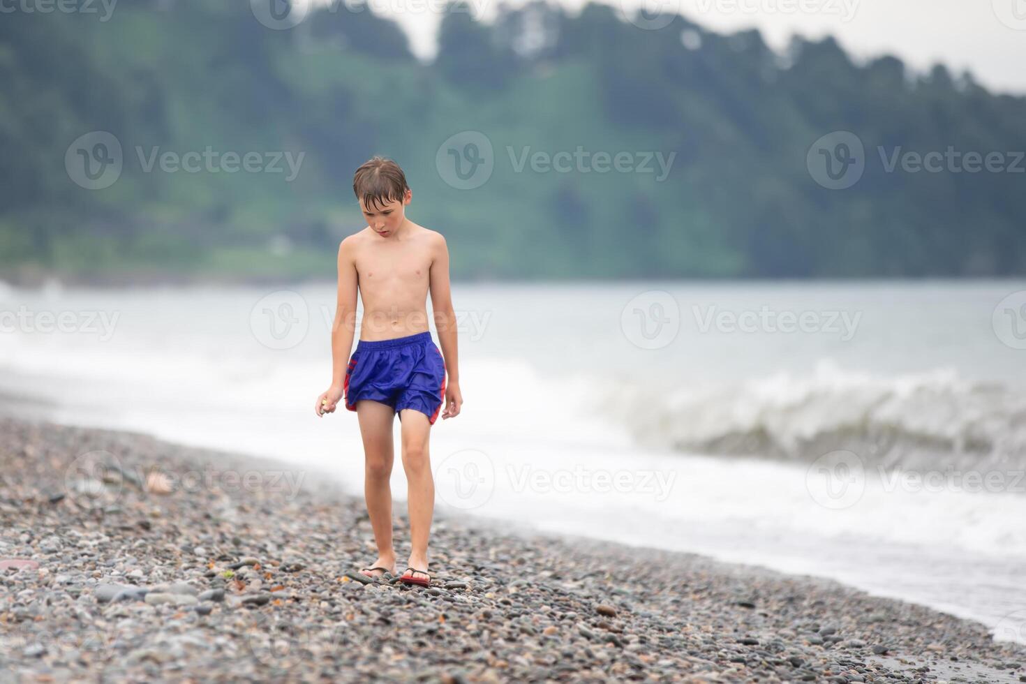 The boy walks along the rocky shore of the sea. photo