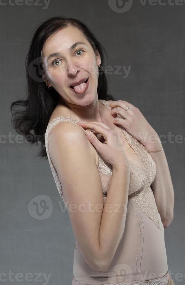 A middle-aged woman in lingerie shows her tongue playfully. photo